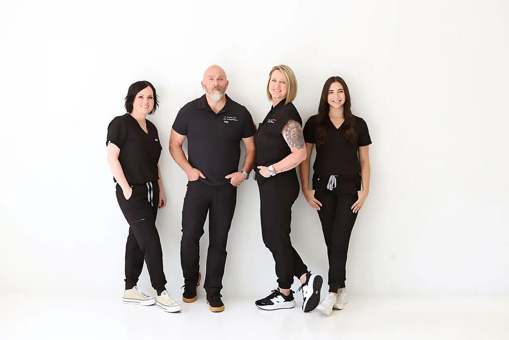Four healthcare professionals in black scrubs pose against a white background, smiling at the camera.